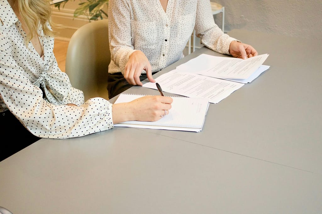 Two women reviewing legal documents and taking notes during a personal injury consultation.
