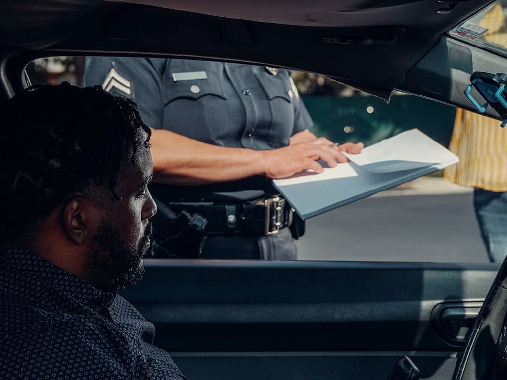 Police officer writing a traffic accident report while a driver looks on – illustrating key evidence for proving fault in an accident claim.