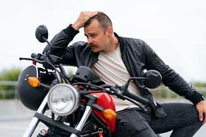 Frustrated motorcycle owner sitting beside red bike after repeated mechanical failures.