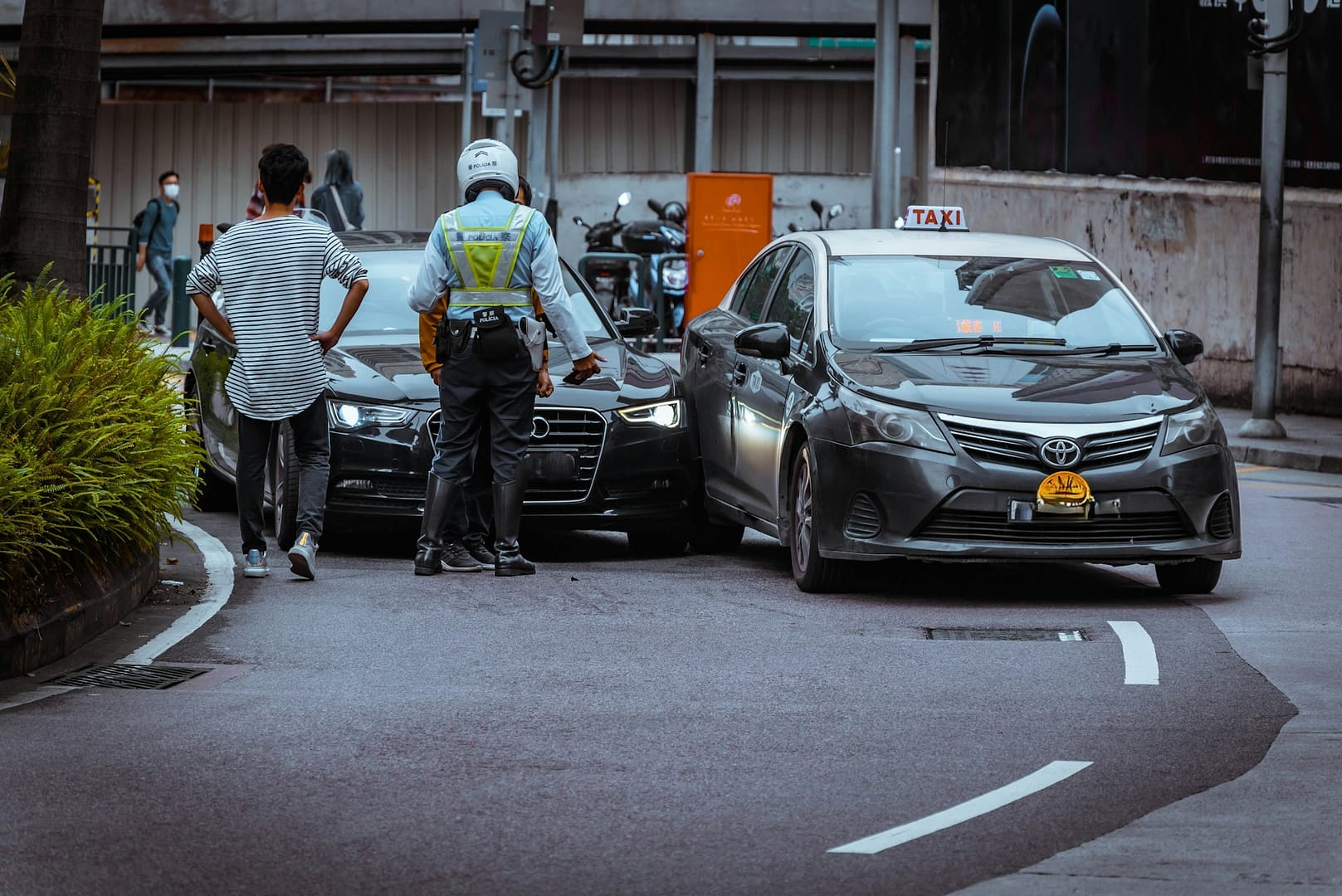 A police officer stands between two cars that have collided on a city street, as two men observe the scene and discuss possible negligence or fault in car accidents.