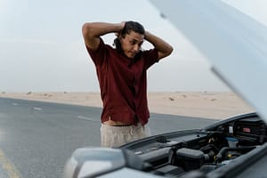 Frustrated driver stranded on the roadside with a defective vehicle, unsure if the issue is covered under warranty or qualifies for legal protection under California’s lemon law