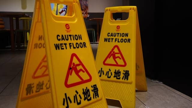 Two yellow caution signs with "Caution Wet Floor" and Chinese text stand on a tiled floor, warning of a potential slip hazard—an important reminder to seek advice from a slip and fall lawyer if accidents occur.